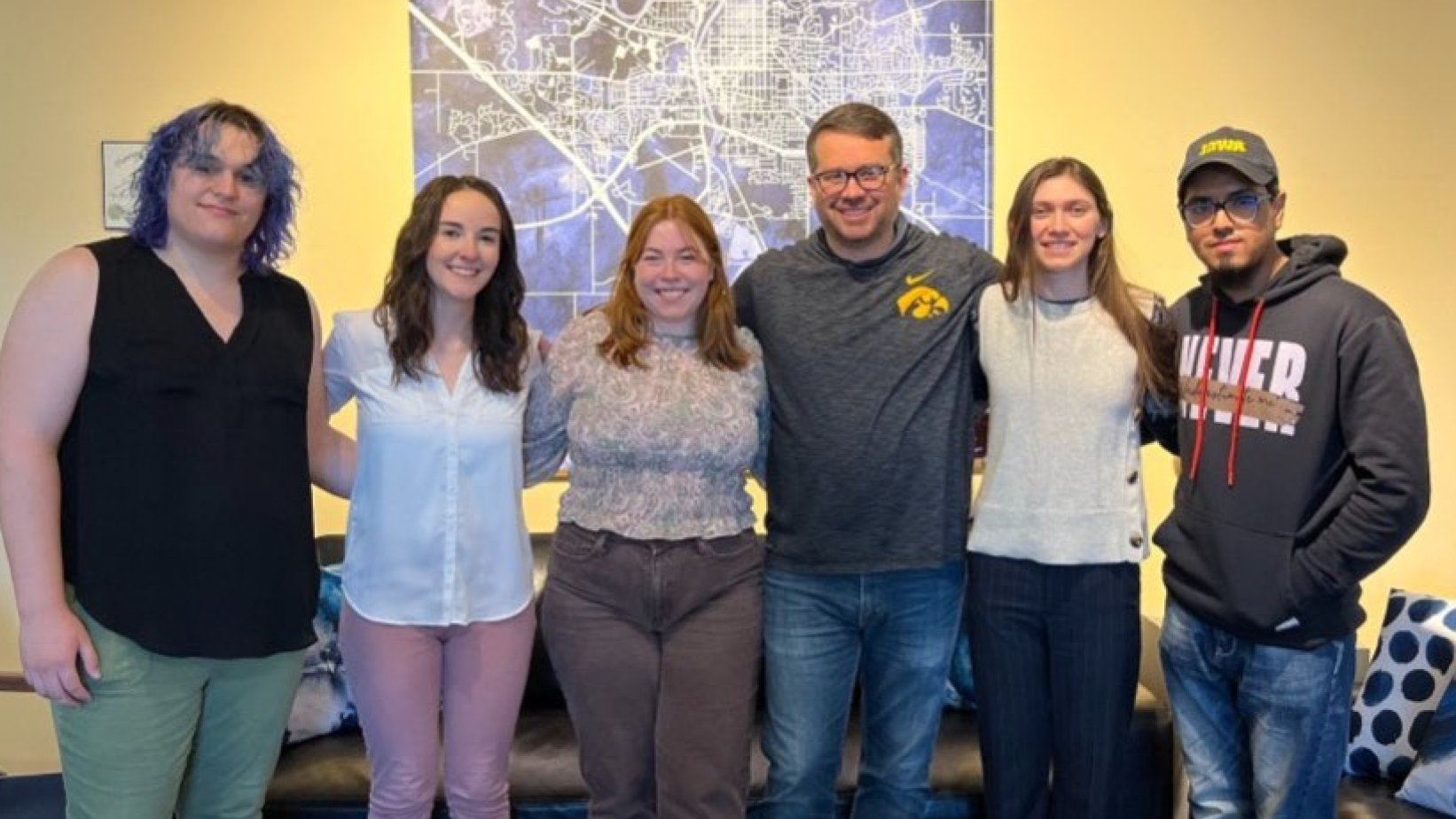 Group of six young adults standing in front of a map. 