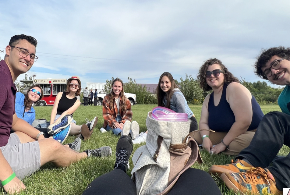 A group of young adults sitting on a blanket outside. 