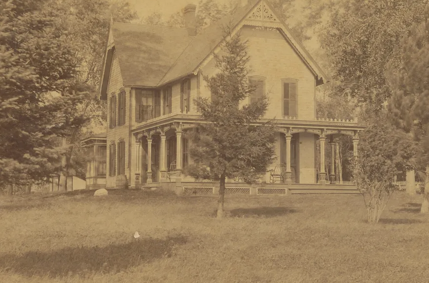 old yellowed photo of large white wooden house on what appears to be a large, open plot of land.