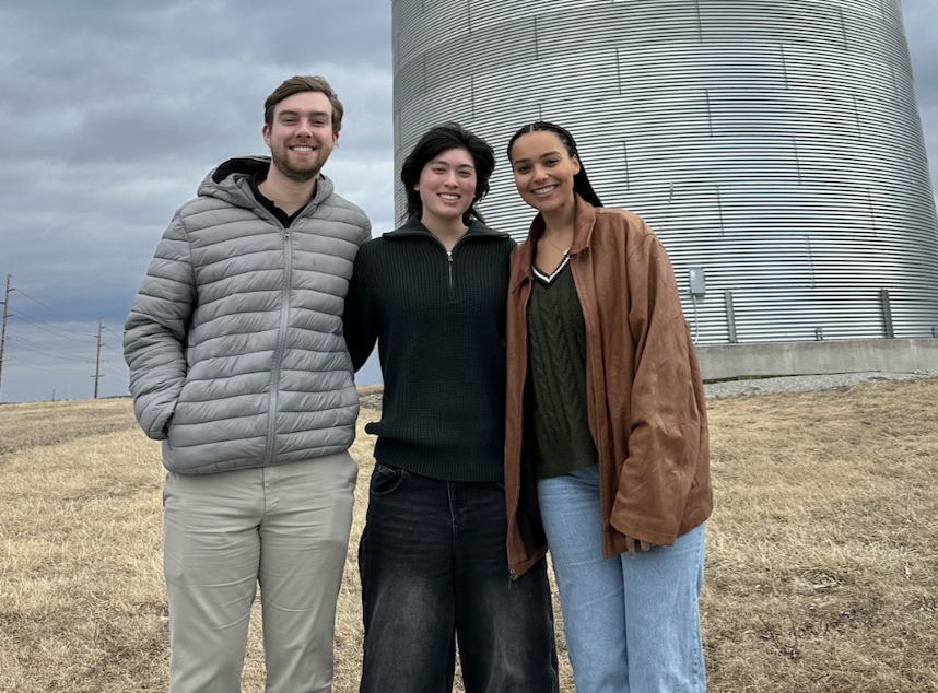 three young people standing outside in front of a grain silo