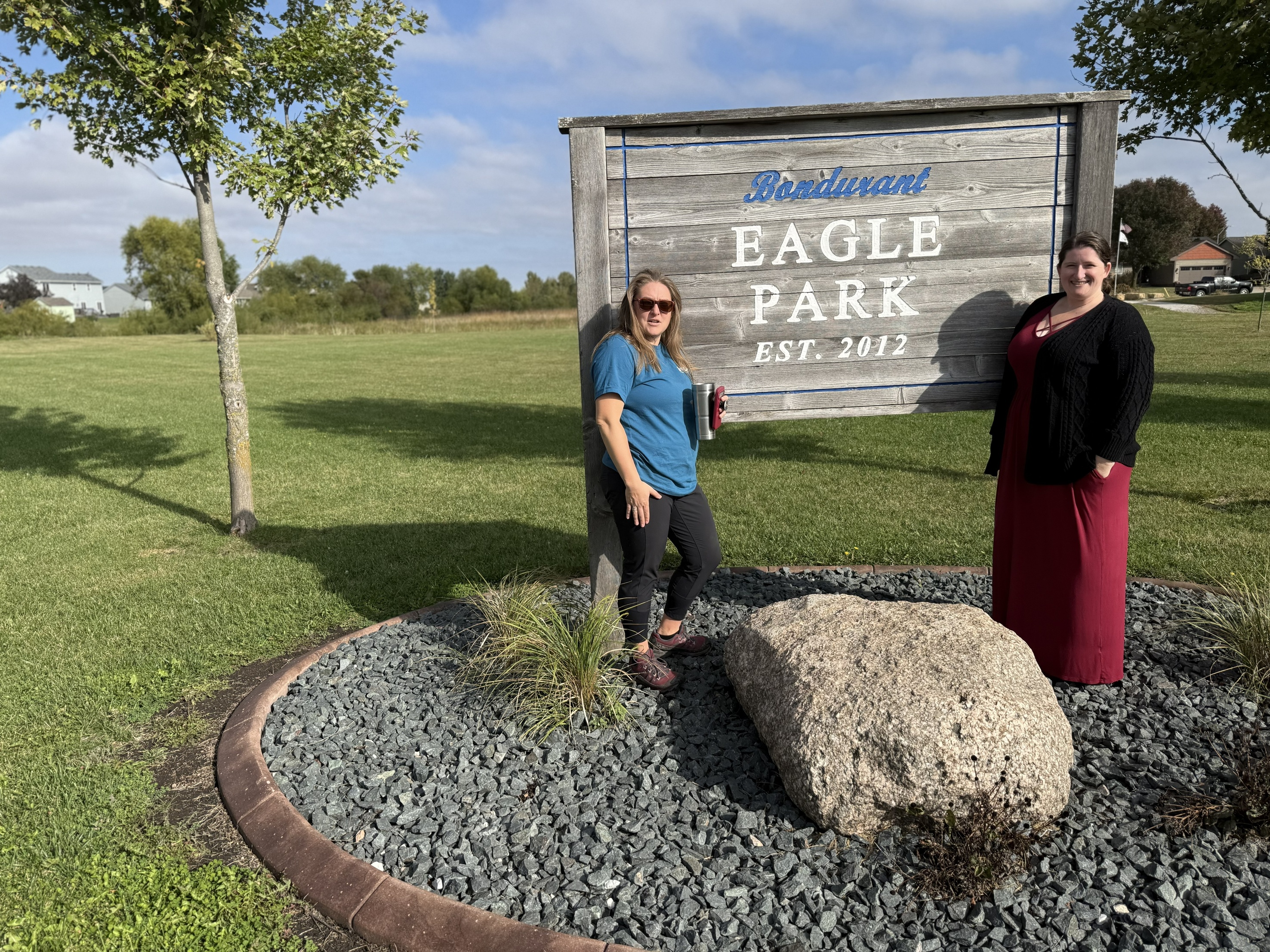 Two women pose at the entrance to a park next to a sign that says Eagle Park.