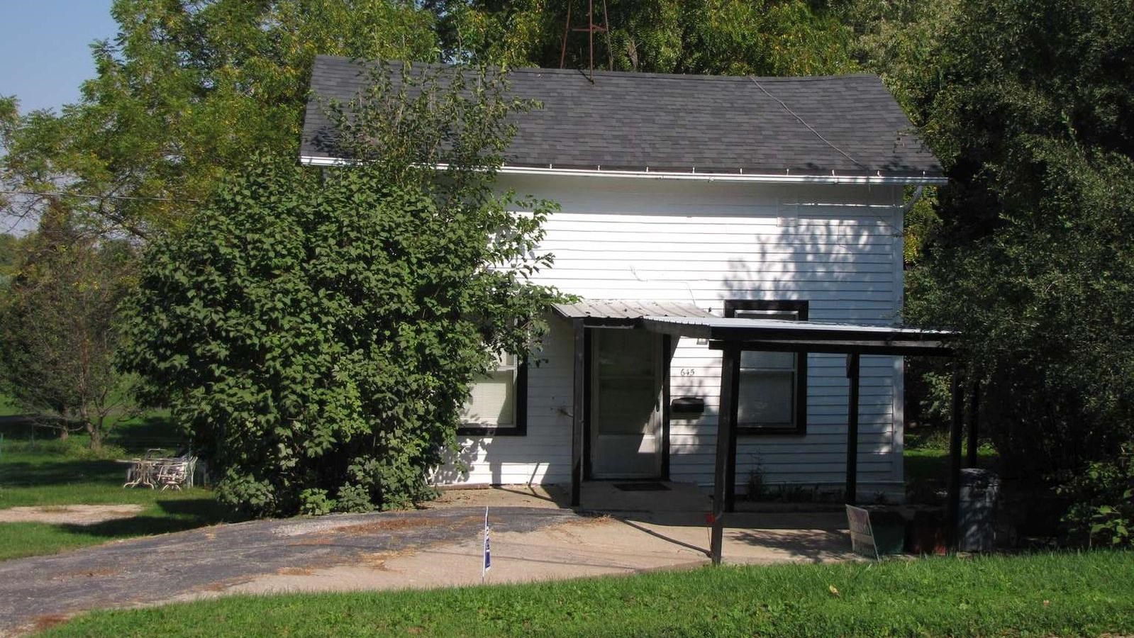 A simple white house surrounded by bushes and trees.