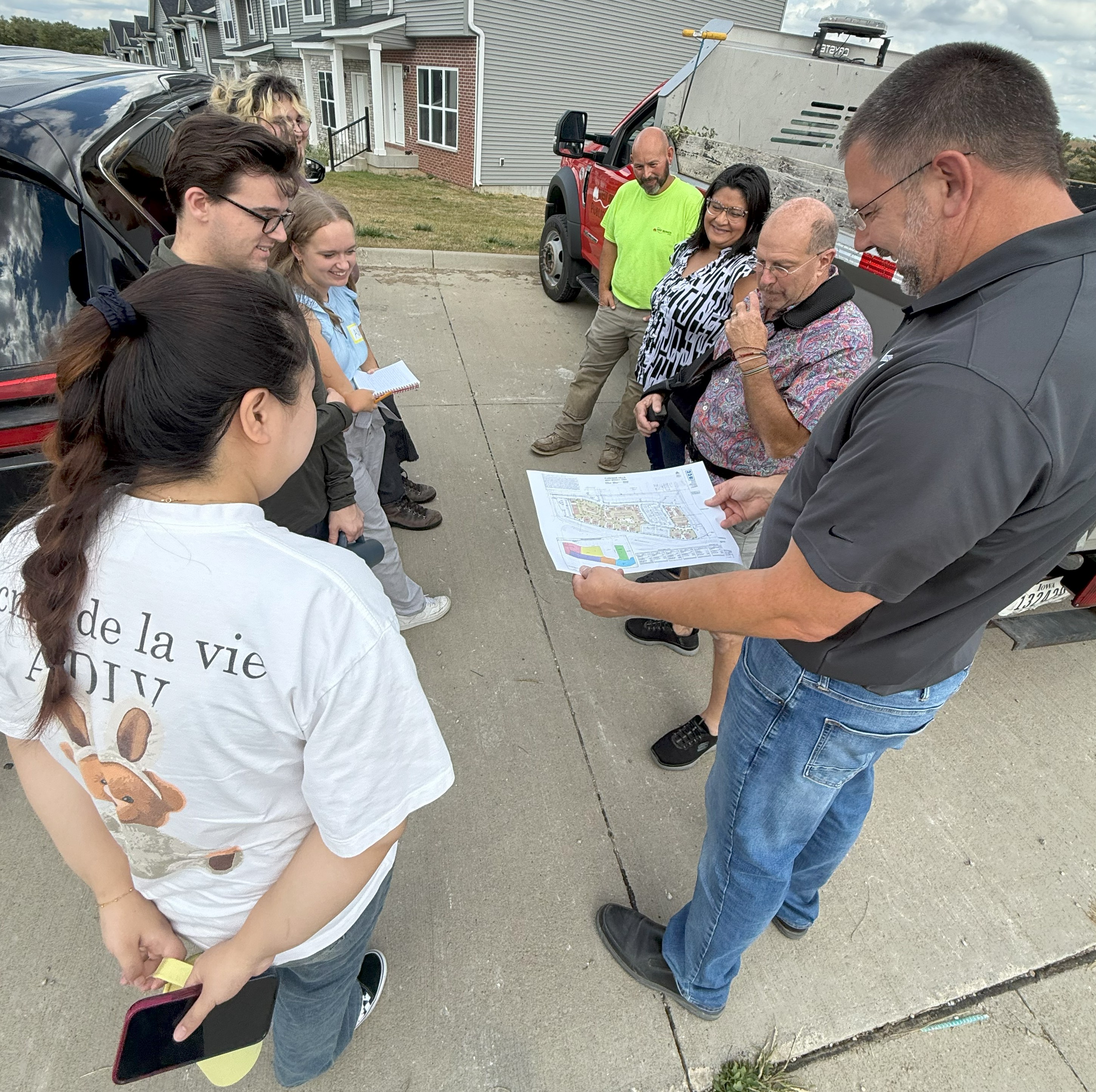 A group of six people stand in a circle looking at a map held by one man