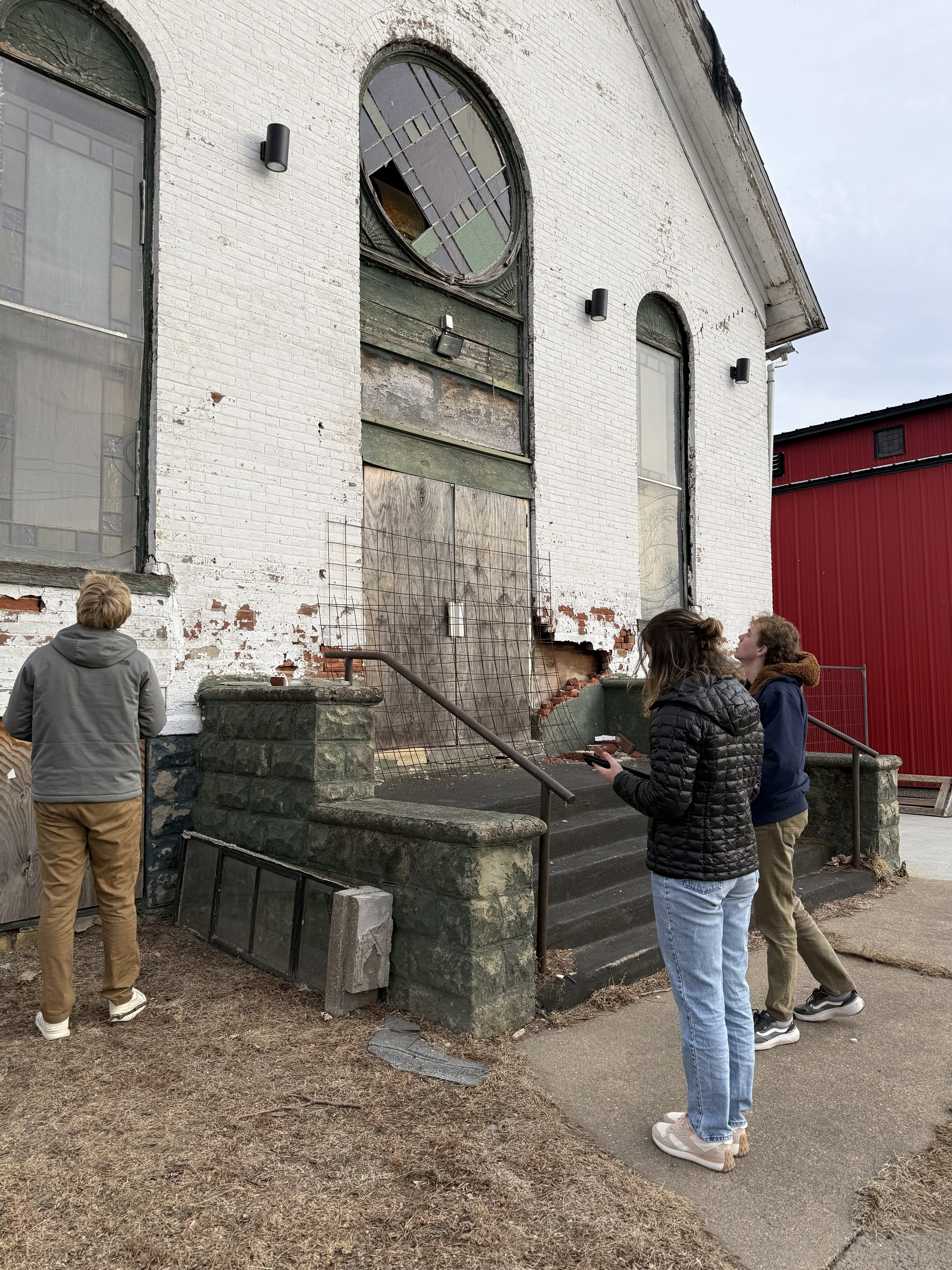 Two students measure dimensions while standing outside of a white church building.
