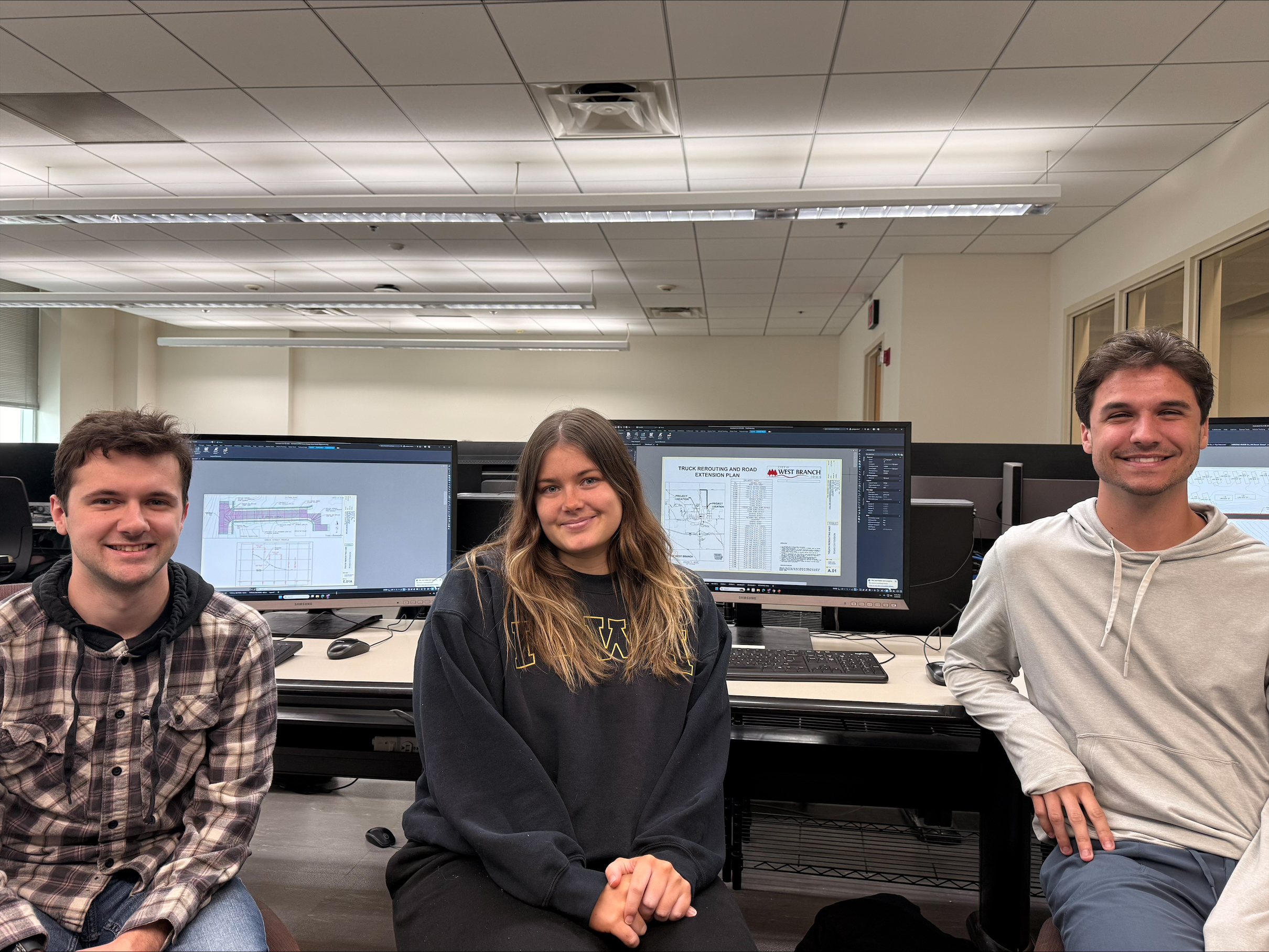 Three students sit smiling in a computer lab