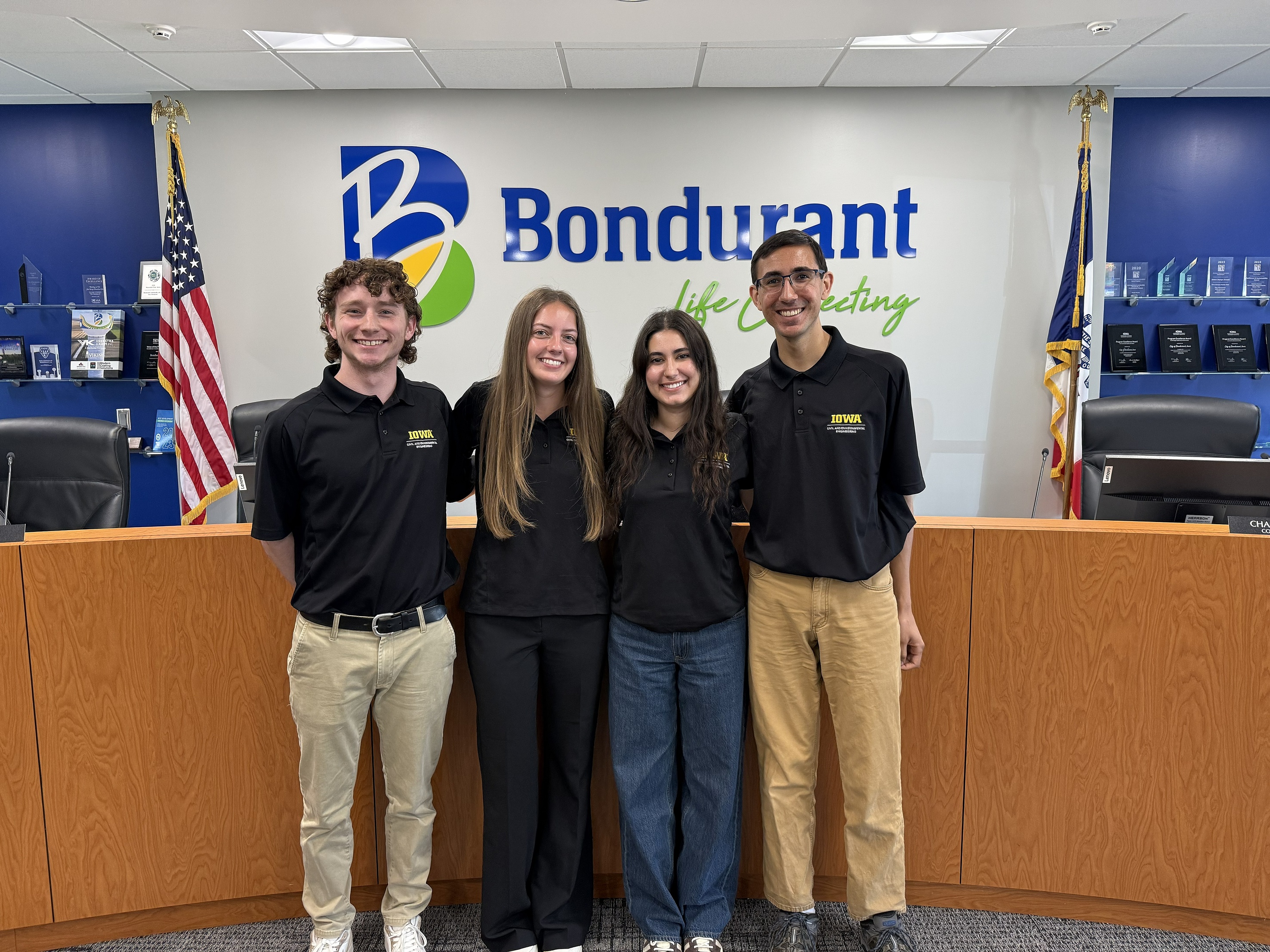 Four students wearing Engineering polos smile at the camera while standing in the Bondurant City Council Chambers.