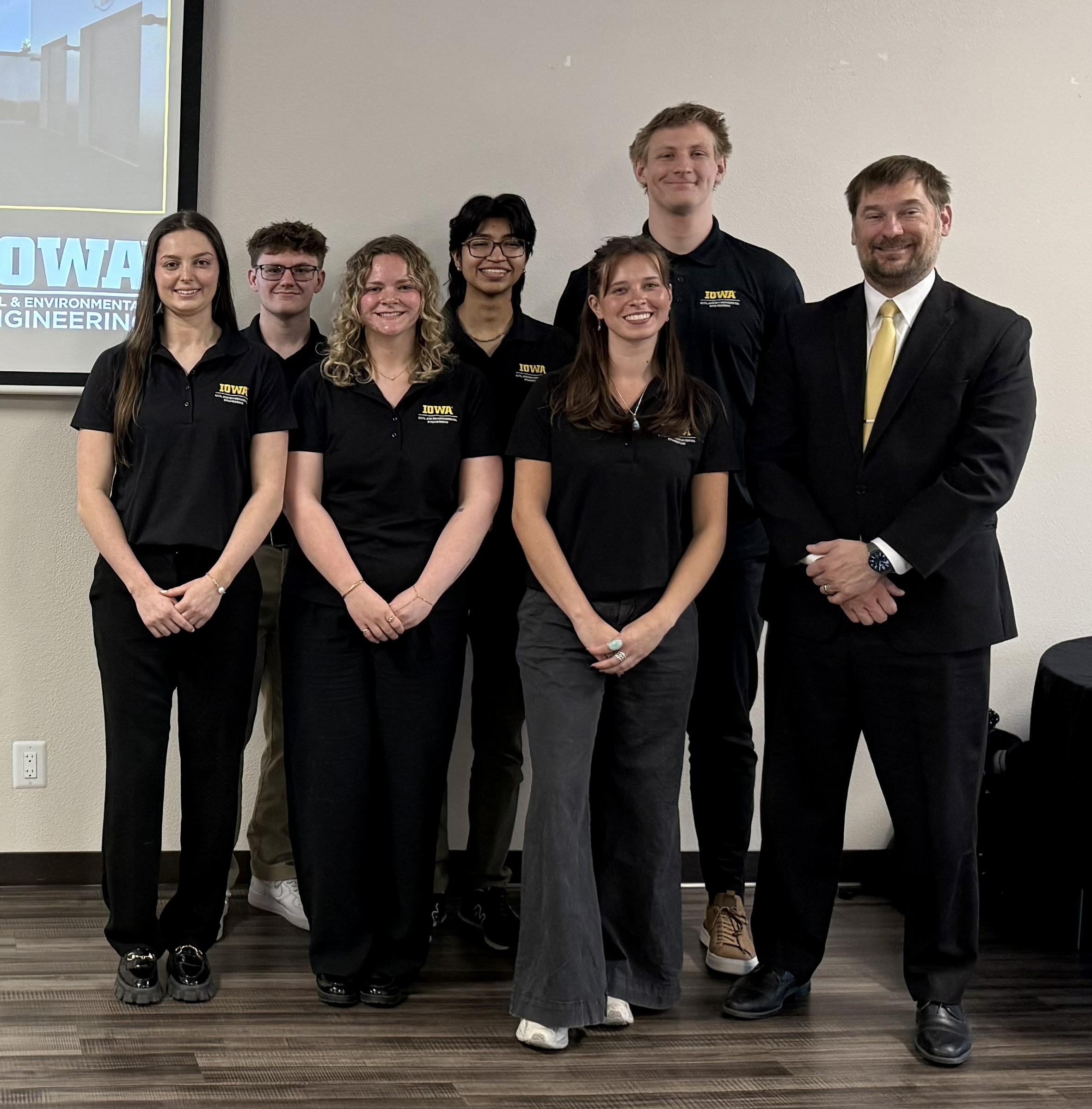 Students wearing Engineering polo shorts stand along with their faculty member at the front of a room