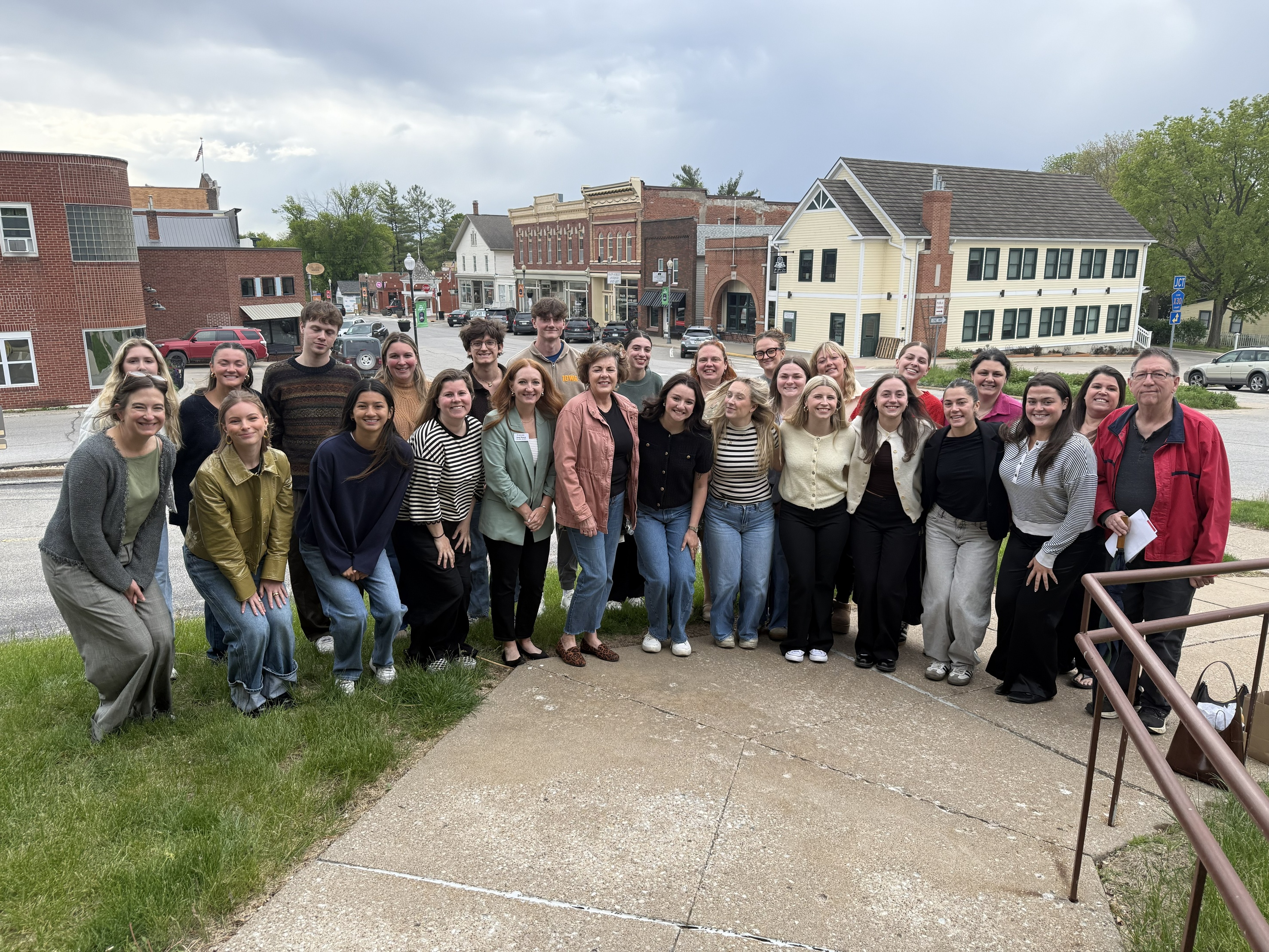 A group of students and community members stand smiling in front of Main Street, West Branch