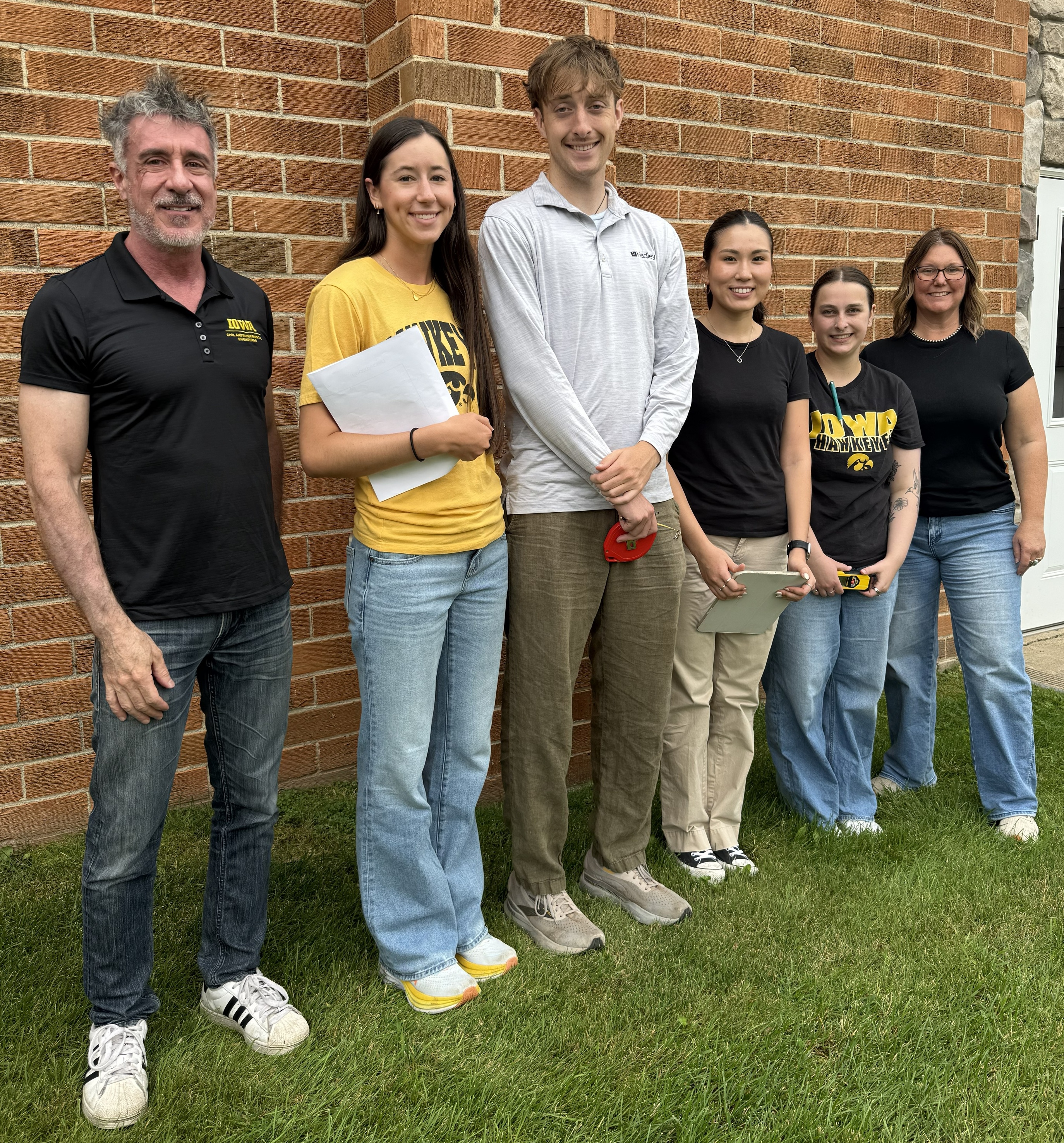 A group of six people standing in front of a brick wall