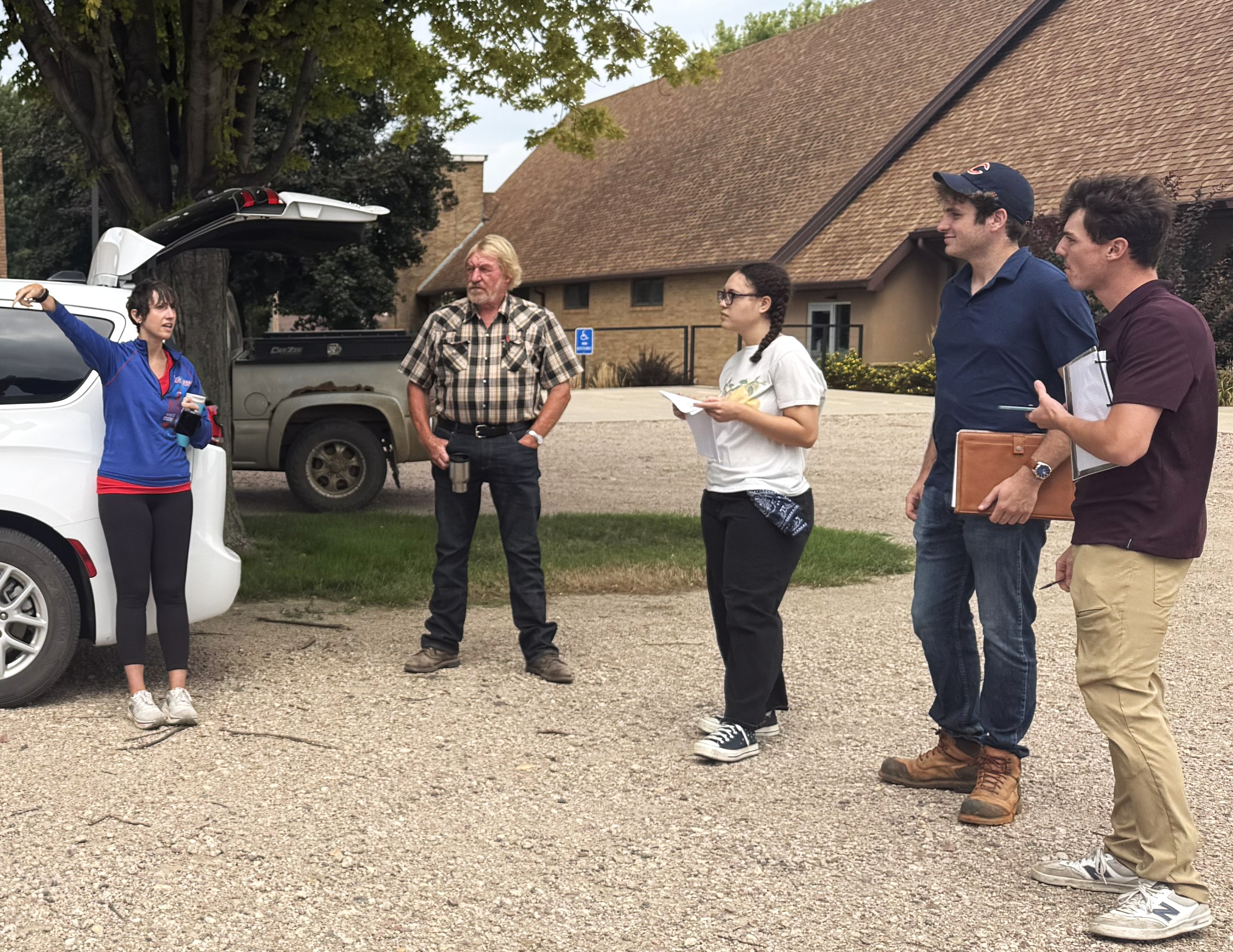 a group of five people talk in a parking lot.