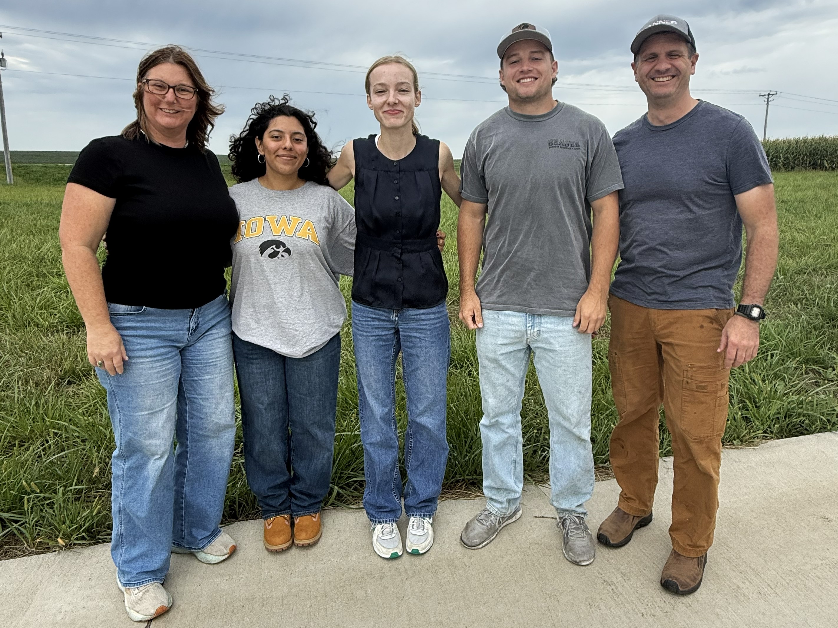 A group of five people stand in front of a field smiling.