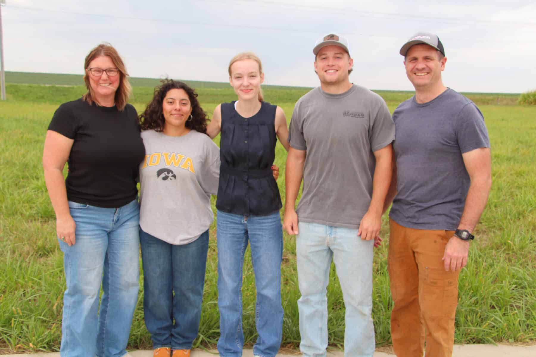 A group of five people stand in front of a field smiling
