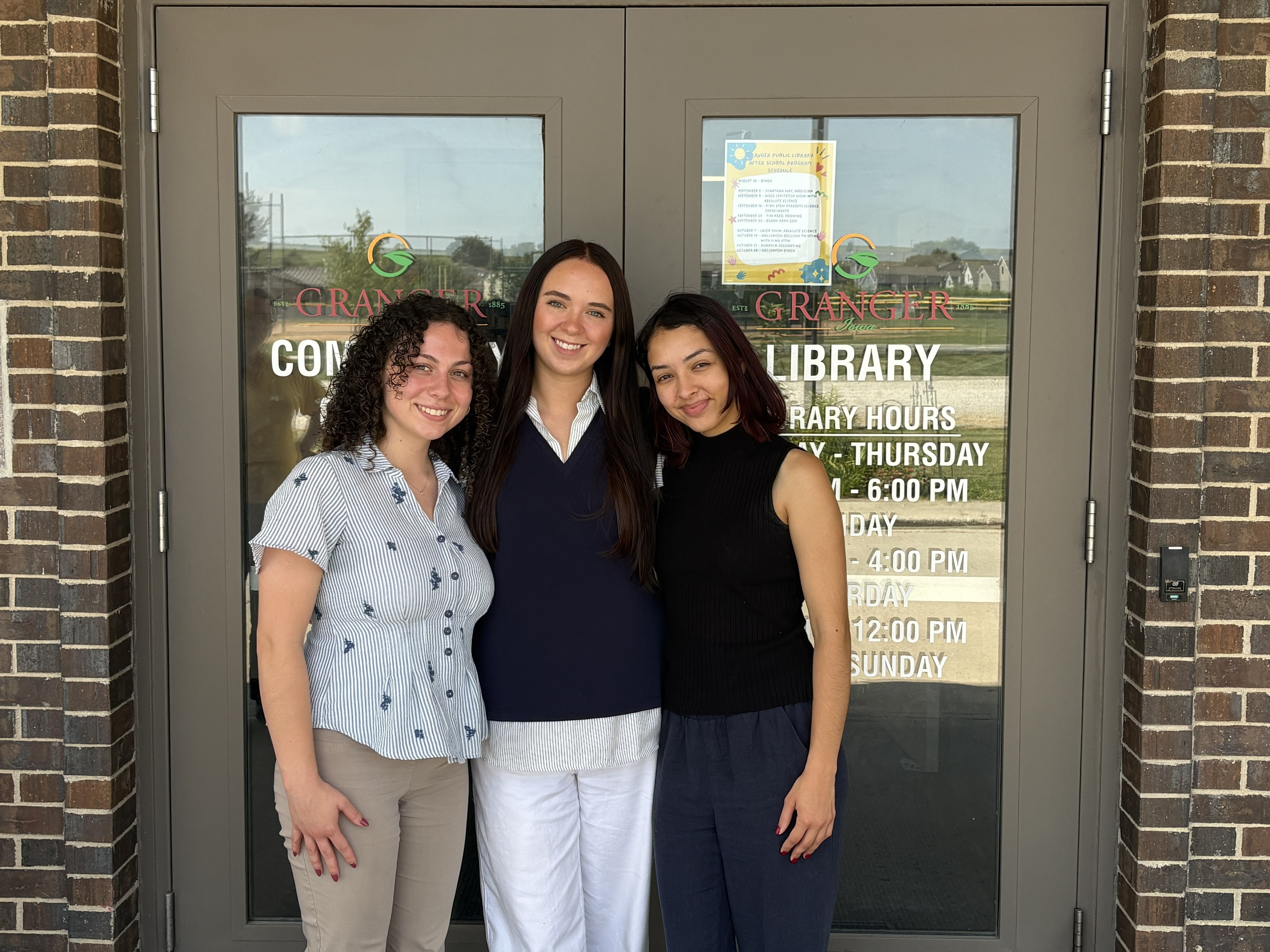 Three people stand smiling in front of the Granger library