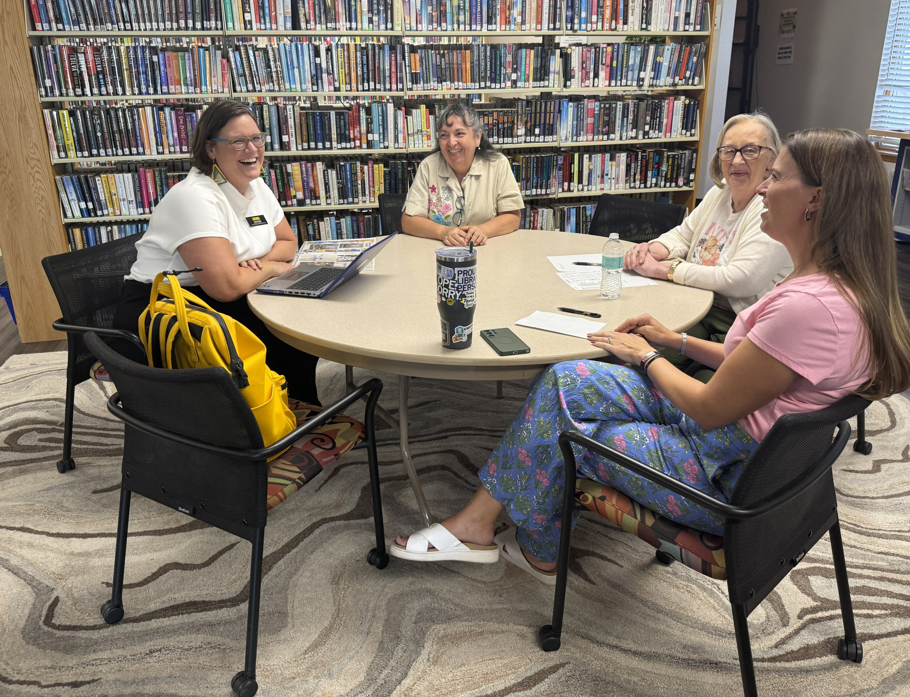 Four women sitting around a table in a library smiling