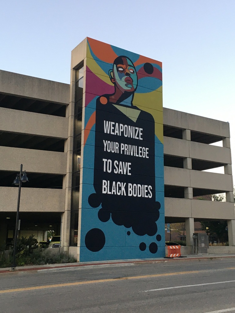 Tall and colorful mural on the side of a parking garage.