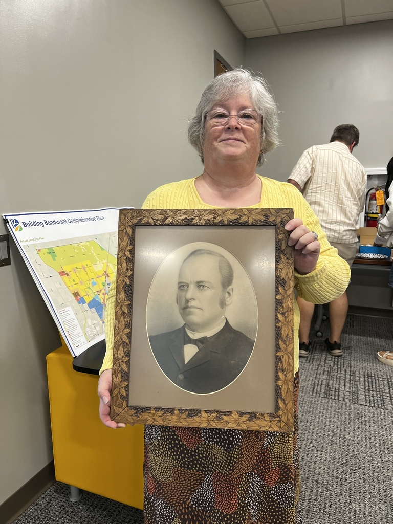 Older woman in yellow sweater holds old black and white portrait of a caucasian man. 