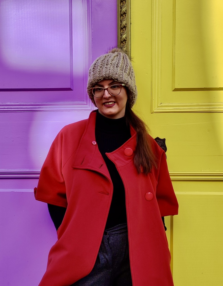 woman in bright red coat stands against brightly painted old doors
