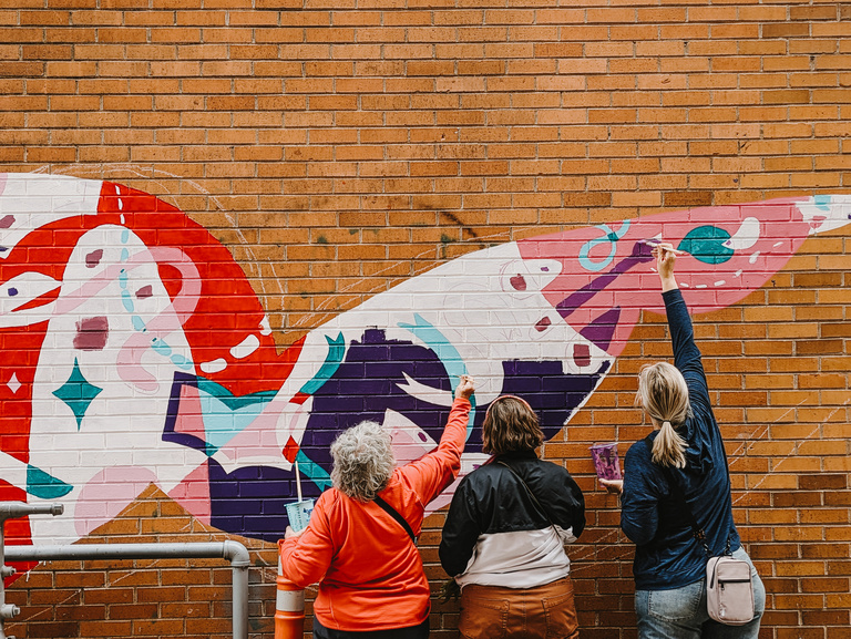 Three women painting on the side of a brick wall.