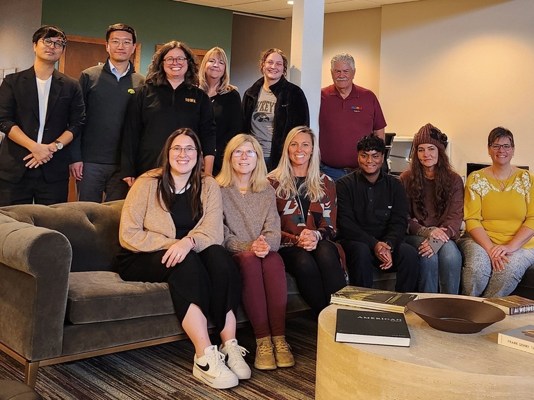 A group of 12 students and community partners sitting and standing smile at the camera