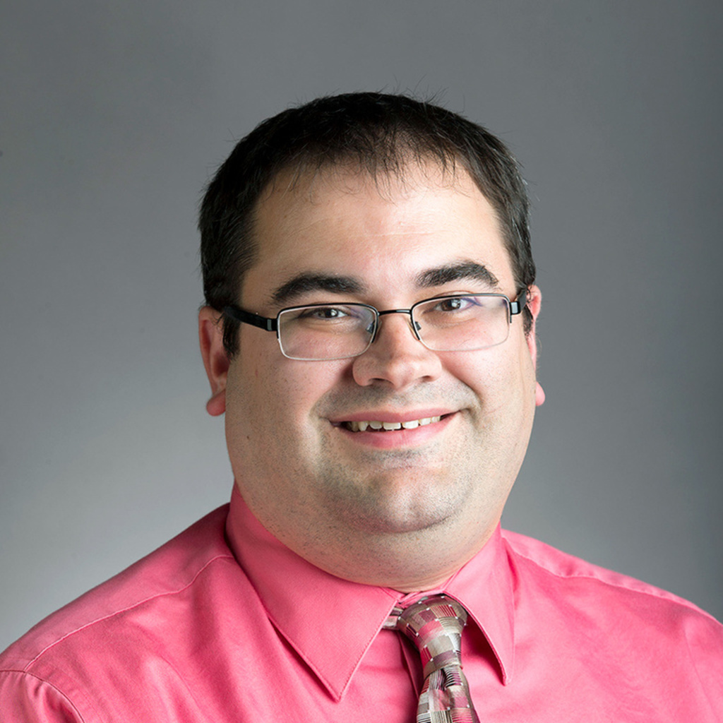 Headshot of a smiling caucasian man wearing glasses in a pink shirt and necktie