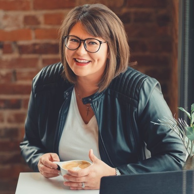 Smiling woman holding a cup of coffee, she is wearing glasses and has brown short hair and white skin