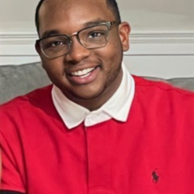 Headshot of young man in bright red shirt, glasses, with black skin