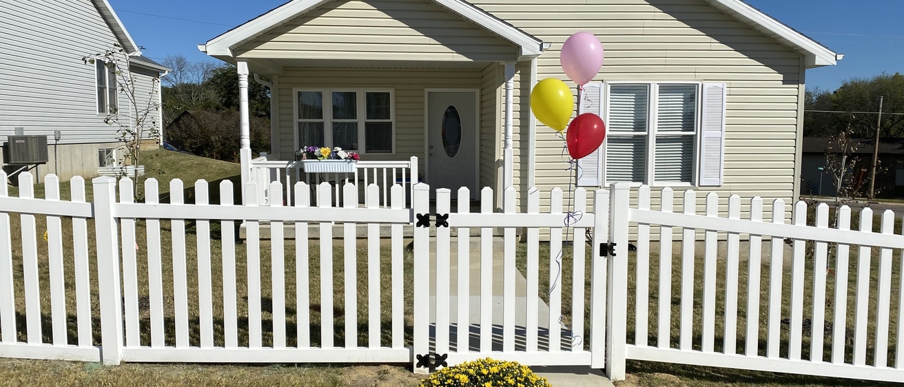 A tan house with a picket fence and balloons outside. 