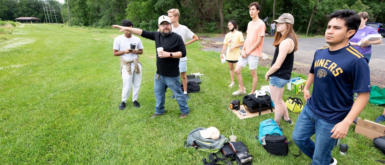 A group stand in a green field holding some scientific instruments. 