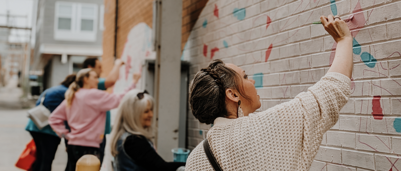 people painting a mural on an outside brick wall