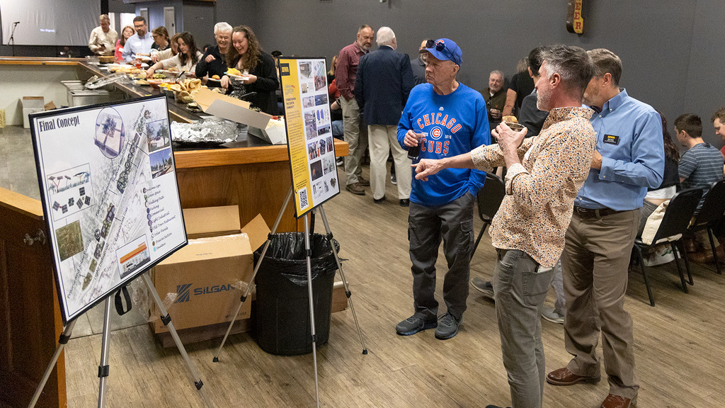 Several people look at academic posters on easels at an indoor public event in a gray room with wood floors.
