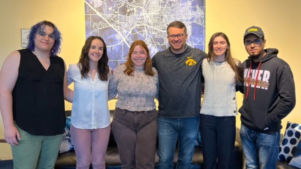 Group of six young adults standing in front of a map.