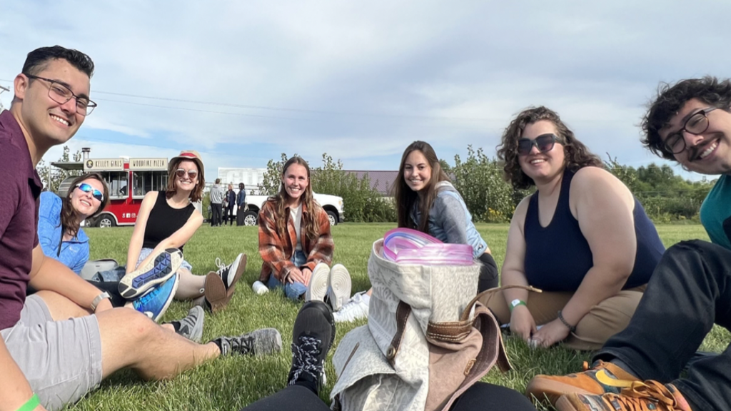 A group of young adults sitting on a blanket outside. 