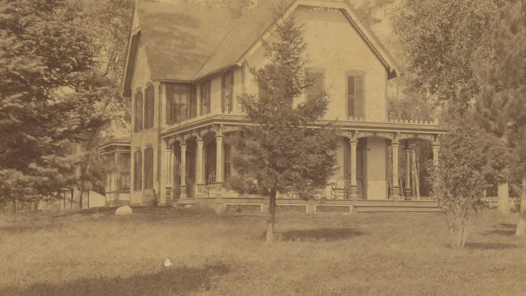 old yellowed photo of large white wooden house on what appears to be a large, open plot of land.