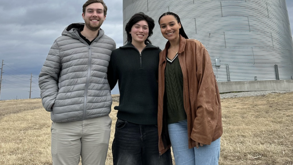 three young people standing outside in front of a grain silo