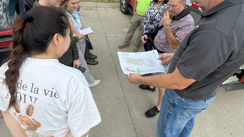 A group of six people stand in a circle looking at a map held by one man