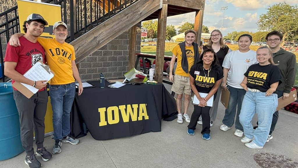 A group of people wearing Hawkeye colors stand around a table with a University of Iowa logo.