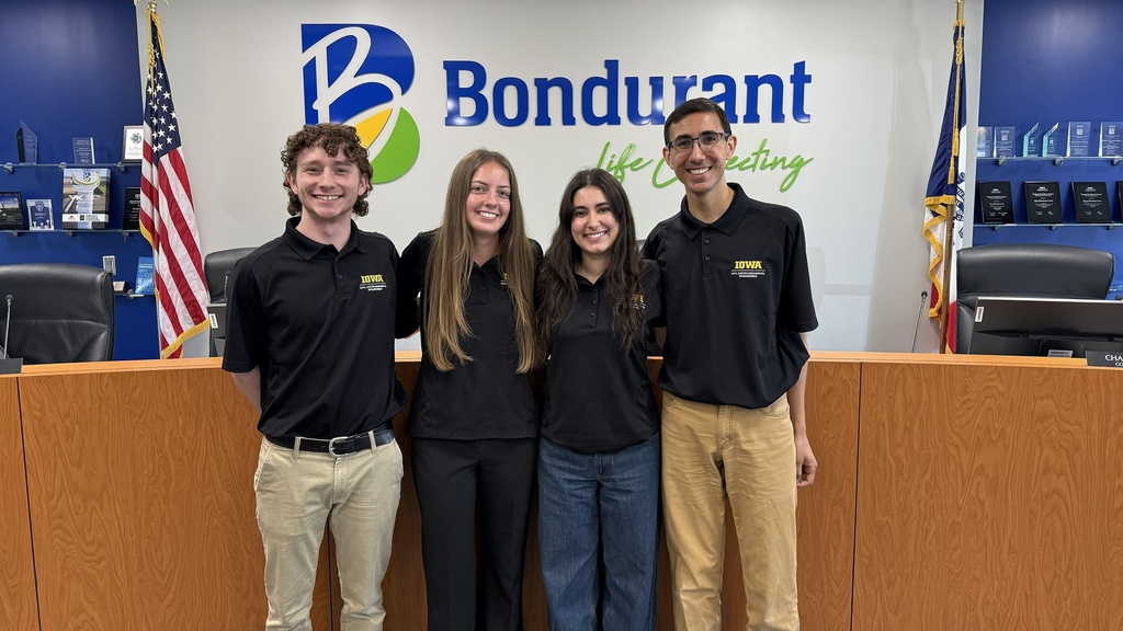Four students wearing Engineering polos smile at the camera while standing in the Bondurant City Council Chambers.
