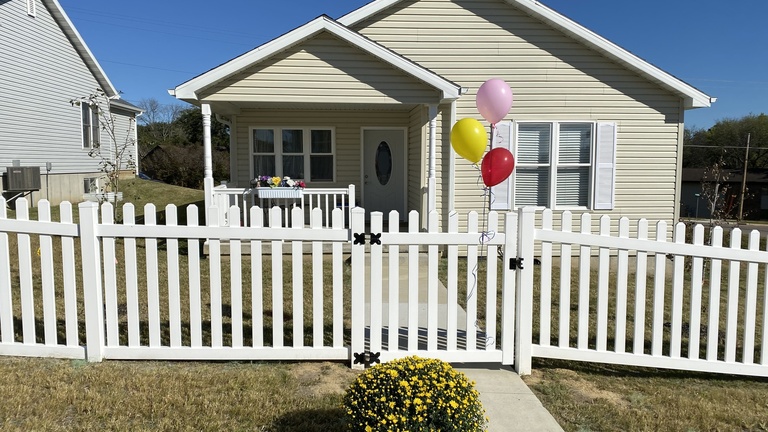 A tan house with a picket fence and balloons outside.