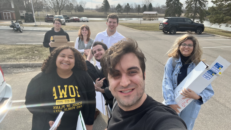 Five people outside holding papers and binders, smiling into the sun.