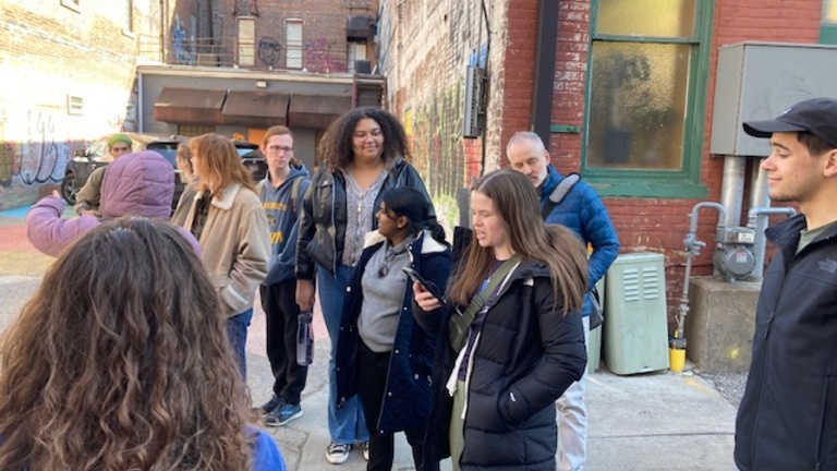 A group of people in an alley that has a lot of graffiti and other art.