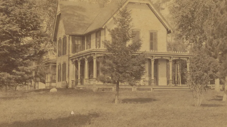 old yellowed photo of large white wooden house on what appears to be a large, open plot of land.