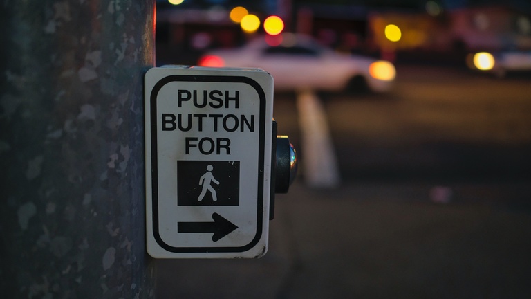 Cross walk button on side of a pole with universal image for a pedestrian.