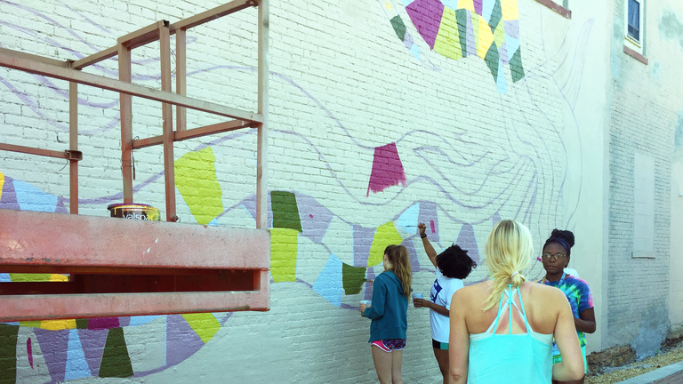 a group of people work on painting a mural on the side of a building.