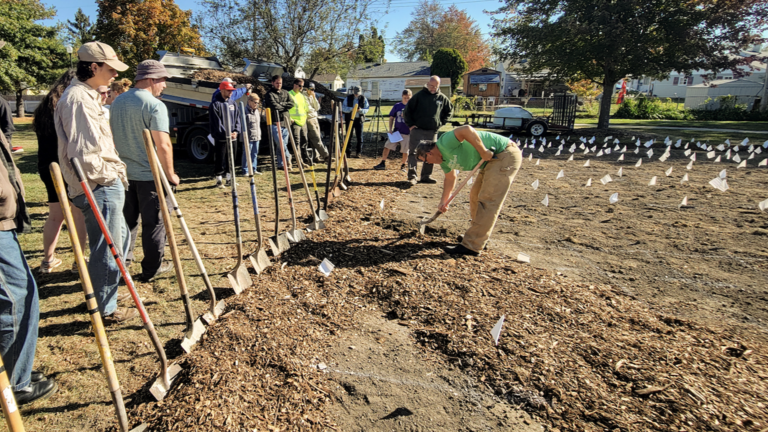 row of young people with shovels and freshly tilled dirt